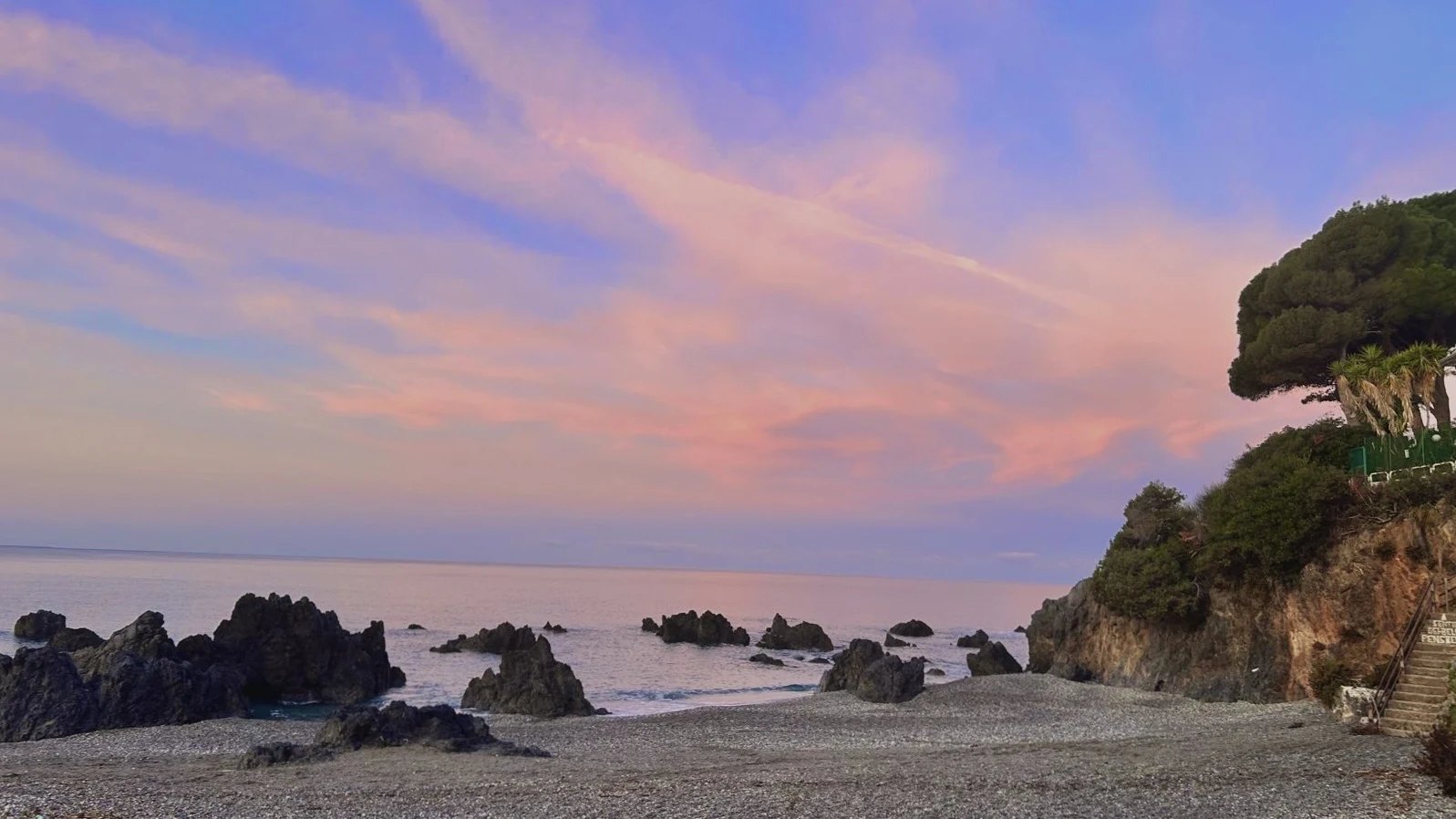 Sunset over the sea at Scalea: rocks, a shingle shore and pines on the cliff